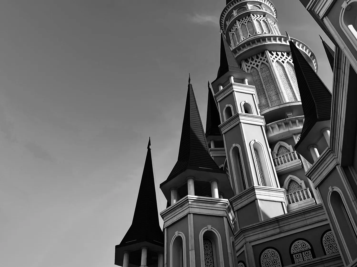 Černobílý pohled vzhůru na špičaté věže zámku, s kulatou věží zdobenou oblouky proti zamračené obloze